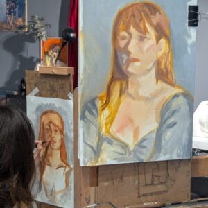 Deux portraits à la peinture à l'huile d'une femmes rousse sur fond bleu gris une artiste est en train de desssiner la bouche sur sa peinture