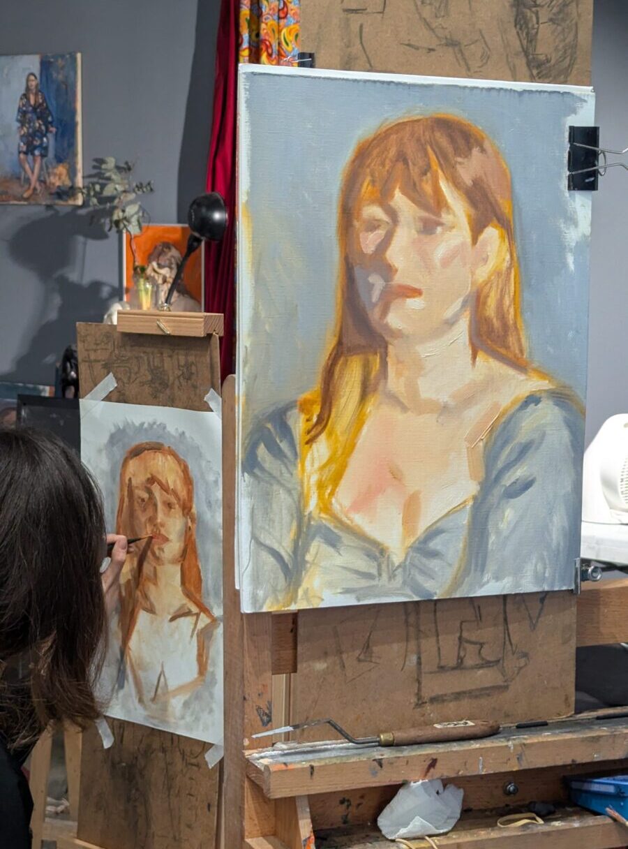 Isaline au stage portrait Deux portraits à la peinture à l'huile d'une femmes rousse sur fond bleu gris une artiste est en train de desssiner la bouche sur sa peinture
