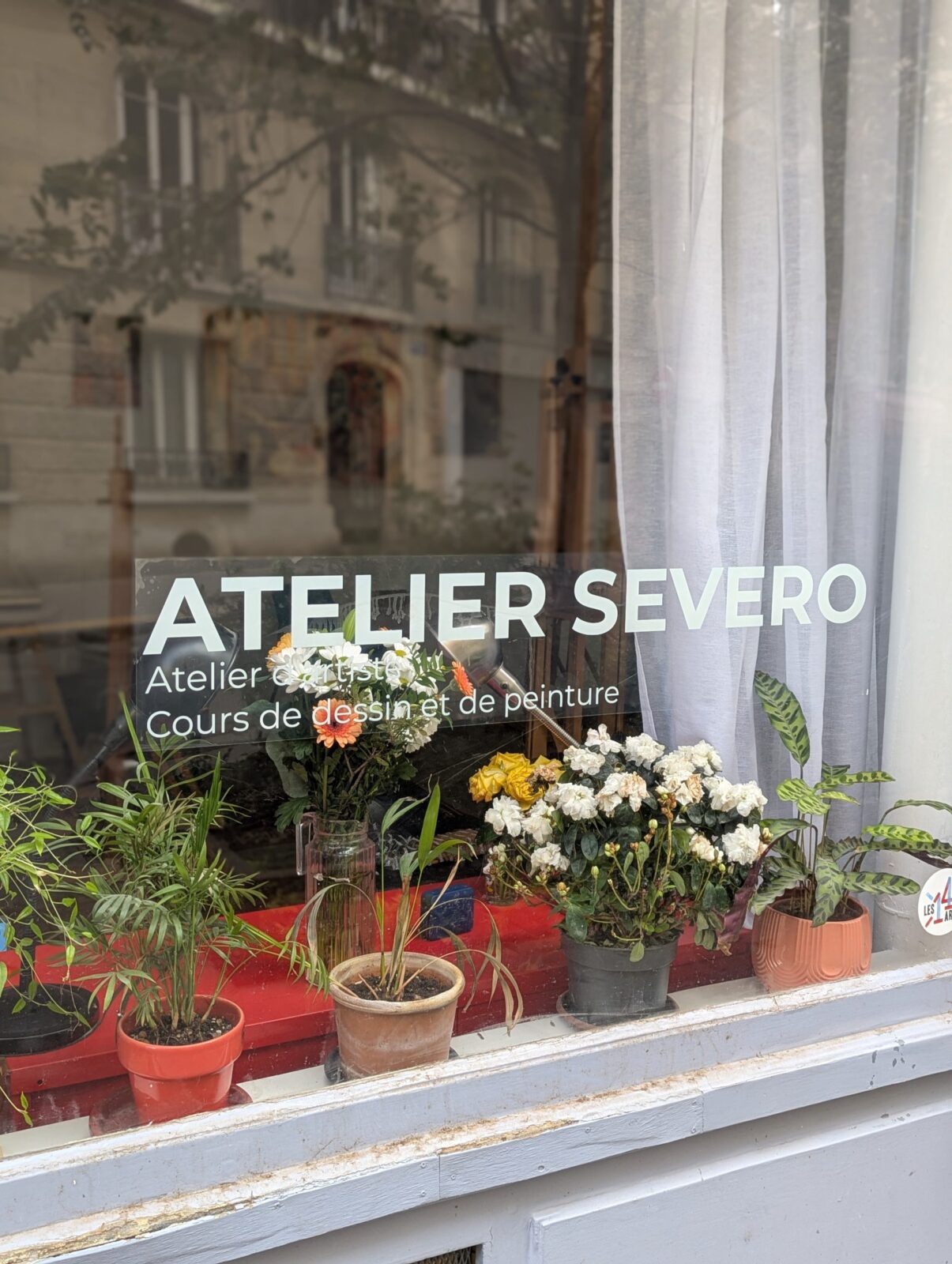 Photo de la vitrine de l'Atelier Severo, avec l'enseigne Atelier Severo — Atelier d'artiste, Cours de dessin et de peinture, et un chevalet visible à travers la vitre